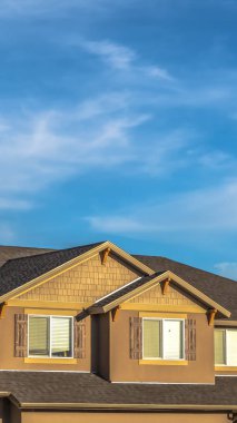 Vertical House exterior with dormers and gray roof against hills and cloudy blue sky