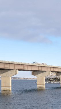 Dikey çerçeve Stringer köprüsü göl arazisi ve bulutlu gökyüzü gibi görünen katmanlarla desteklenmektedir.