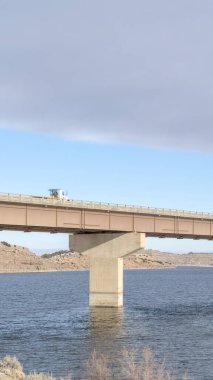 Tepelerin manzarası ve kışın bulutlu mavi gökyüzü olan bir göl üzerindeki dikey köprü.