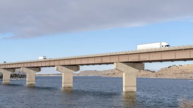 Panorama Büyük kamyonlar karlı tepelere ve bulutlu gökyüzüne karşı büyük bir köprüde seyahat ediyorlar