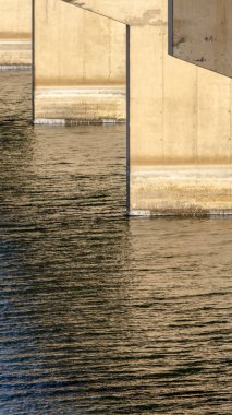 Dikey çerçeve, bir kiriş köprüsünün altında güneşli göl suyuna karşı ayaklarıyla görüntüler