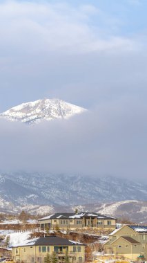 Fotoğraf dikey çerçeveli evler kışın kalın bulutlara karşı karlı bir dağ zirvesi manzaralı