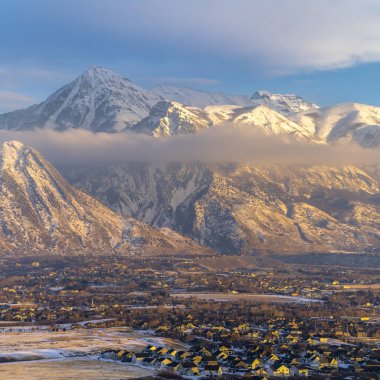Fotoğraf Meydanı Karlı Timpanogos Dağı ve bulutlu mavi gökyüzüne karşı büyüleyici evler gün batımında