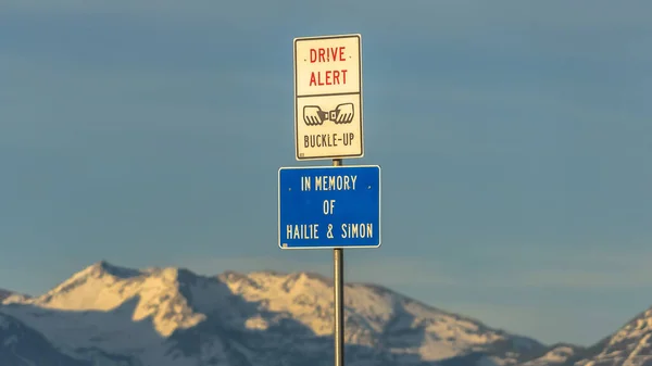 Ramka panoramiczna Drive Alert i Buckle Up znak drogowy przed śnieżną górą i zachmurzone niebo — Zdjęcie stockowe