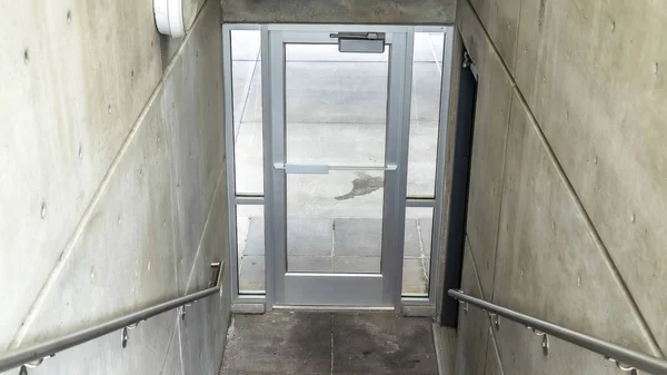 Panorama Staircase inside a building going down to a glass door that leads to outdoors