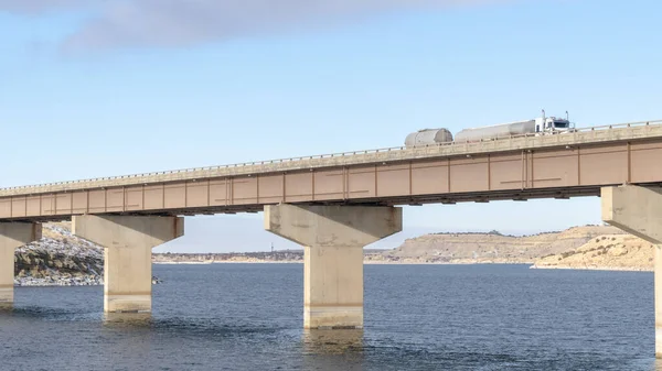 Riesen-LKW auf einer Brücke, die unter wolkenverhangenem Himmel einen blauen See überquert — Stockfoto