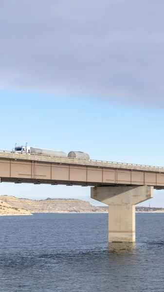 Riesiger LKW auf einer Brücke, die unter wolkenverhangenem Himmel einen blauen See überquert — Stockfoto