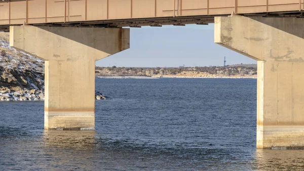 Marco panorámico Enfoque en un puente de viga apoyado por pilares sobre el lago azul contra el cielo nublado —  Fotos de Stock