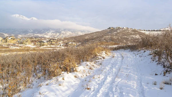 Panorama cadre Route sur colline avec vue sur la neige maisons et montagne contre ciel nuageux — Photo