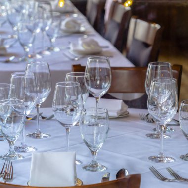 Fotoğraf kare çerçeveli şarap kadehleri çatal kaşıklar tabak tabakları ve beyaz kumaşlı peçeteler.