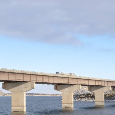 Kare çerçeve Stringer köprüsü, göl arazisi ve bulutlu gökyüzü gibi görünen katmanlarla destekleniyor