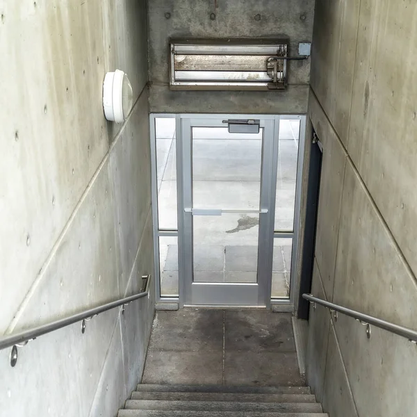 Square frame Staircase inside a building going down to a glass door that leads to outdoors — 스톡 사진