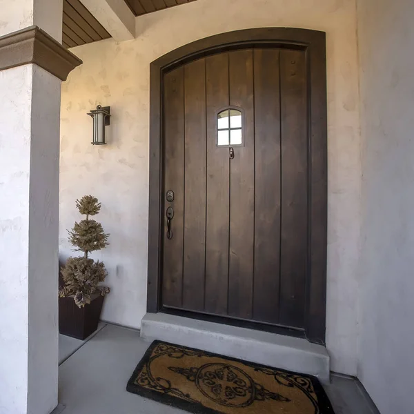 Square Brown wood arched front door with glass panes at the facade of home with porch