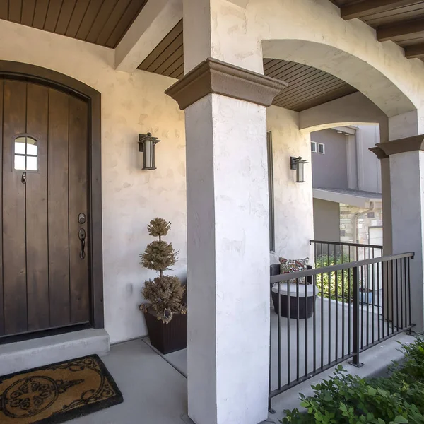 Square frame Brown wood arched front door with glass panes at the facade of home with porch