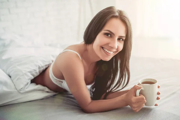 Mujer está acostada en la cama con té — Foto de Stock