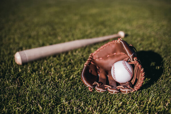 Бейсбольная бита, мяч и перчатка лежат на зеленой траве
