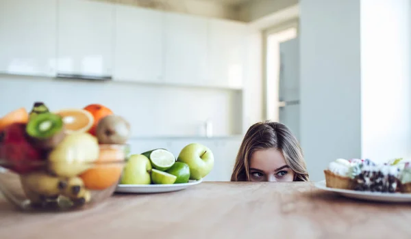 Young woman choosing between fruits and sweets — Stock Photo, Image