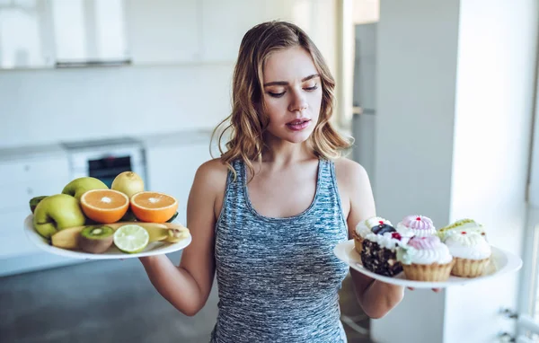 Young woman choosing between fruits and sweets — Stock Photo, Image