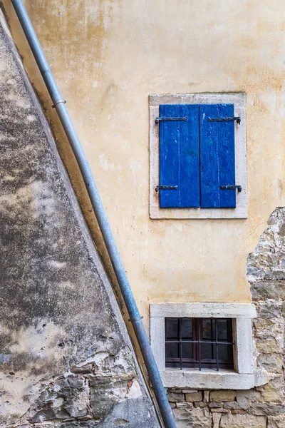 Et gammelt vindu med blå vinduslemmer på steinveggen . – stockfoto