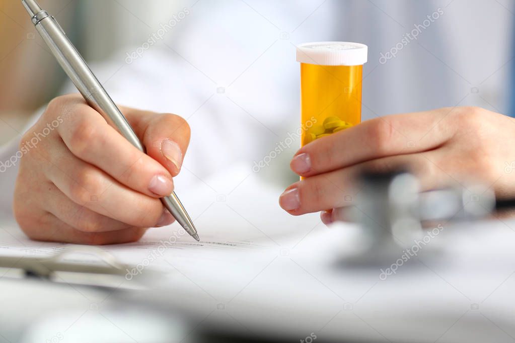 Female doctor hand hold jar of pills and write prescription
