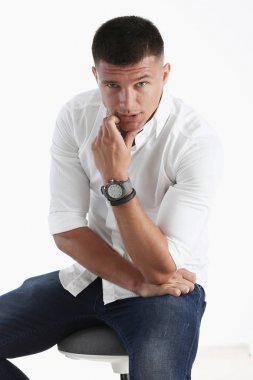 Bir adam elini çenesine için beyaz bir arka planda tutar. Kameraya bakmak gibi davranarak