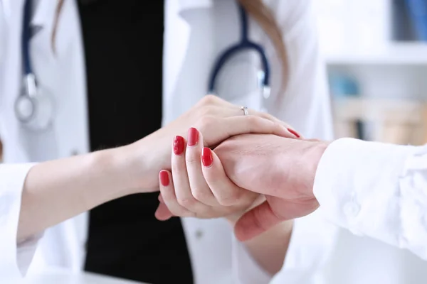 Дружелюбная женщина-врач держит пациента за руку в офисе — стоковое фото