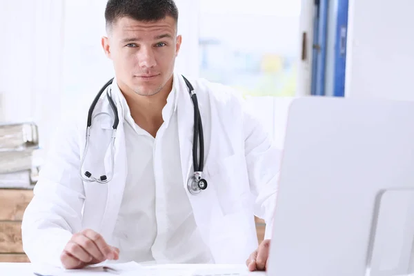 Handsome smiling male doctor write sit at workplace in office — Stock Photo, Image