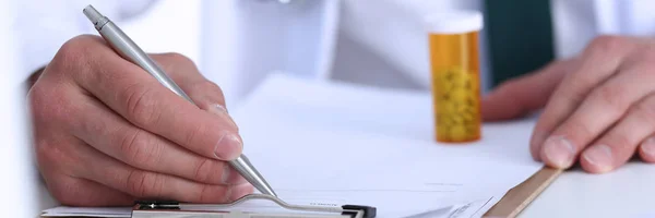 Male doctor hand write prescription at office worktable