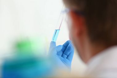 Bir erkek kimyager tüp cam onun el taşmaları tutar.