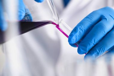 Bir erkek kimyager tüp cam onun el taşmaları tutar.