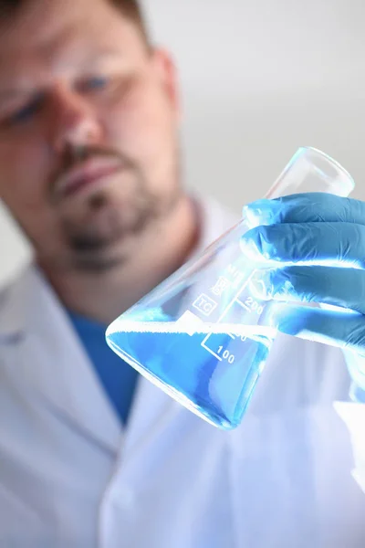 Un químico masculino sostiene tubo de ensayo de vidrio en su mano desborda un líquido — Foto de Stock