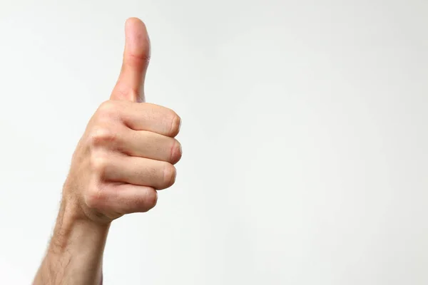 A male hand on a gray background holds a thumb up expressing — Stock Photo, Image