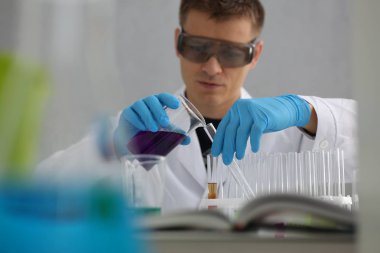 Bir erkek kimyager tüp elinde bardak sıvı bir çözüm taşmaları tutar