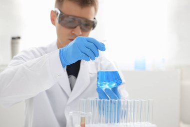 Bir erkek kimyager tüp elinde bardak sıvı bir çözüm taşmaları tutar