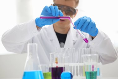 Bir erkek kimyager tüp elinde bardak sıvı bir çözüm taşmaları tutar