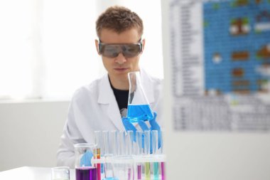 Bir erkek kimyager tüp elinde bardak sıvı bir çözüm taşmaları tutar