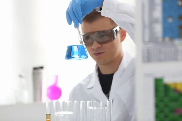 A male chemist holds test tube of glass in his hand overflows a liquid solution — Stock Photo, Image