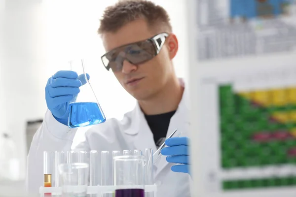 Um químico macho detém um tubo de ensaio de vidro na mão que transborda uma solução líquida — Fotografia de Stock