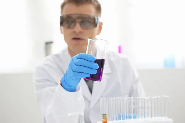 Un chimiste masculin tient dans sa main un tube à essai en verre débordant d'une solution liquide — Photo