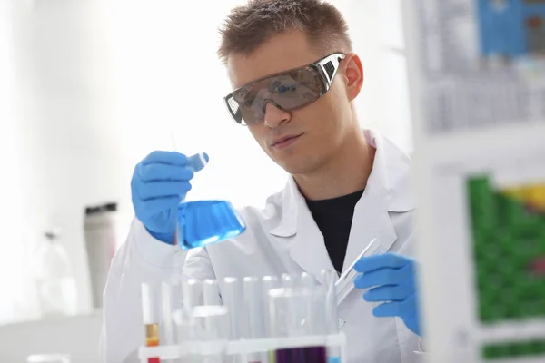 Ένα αρσενικό χημικός κατέχει δοκιμαστικό σωλήνα από γυαλί με το χέρι ξεχειλίζει υγρό διάλυμα — Φωτογραφία Αρχείου