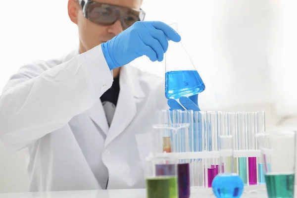 Een mannelijke chemicus houdt reageerbuis van glas in zijn hand loopt over een vloeibare oplossing — Stockfoto