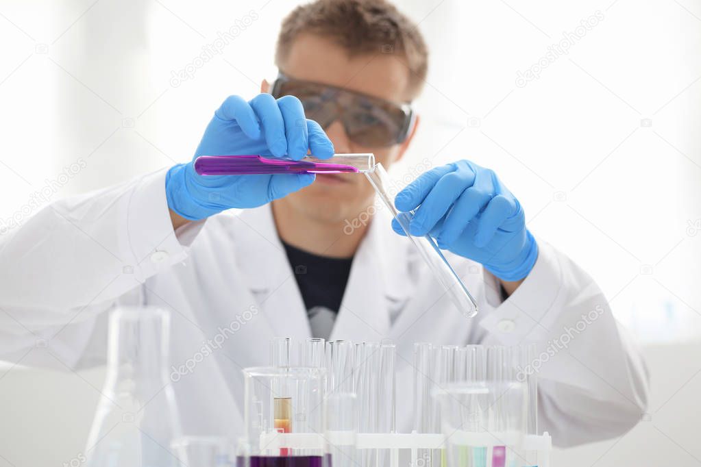 A male chemist holds test tube of glass in his hand overflows a liquid solution