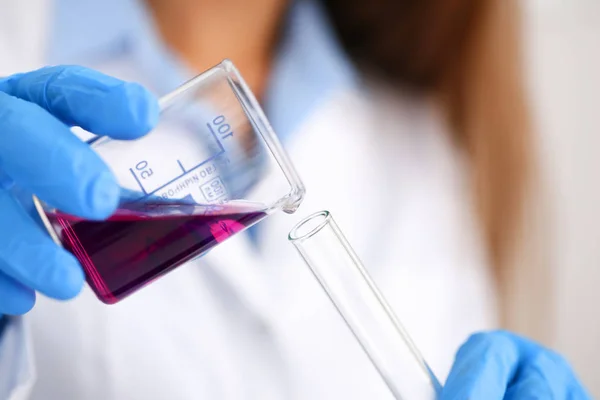 Químico fêmea detém tubo de ensaio de vidro em sua mão transborda um líquido — Fotografia de Stock