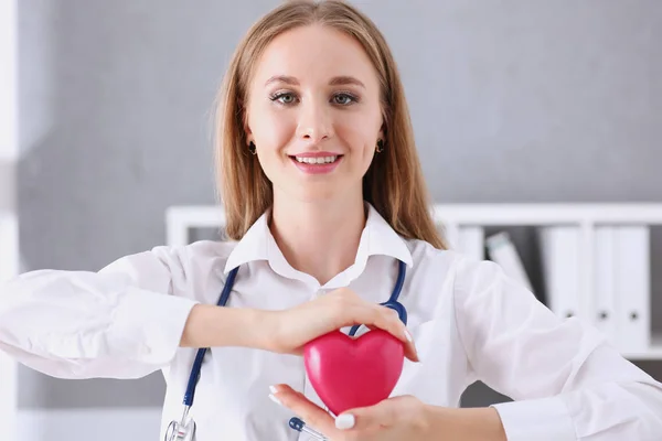Schöne lächelnde Ärztin hält rotes Herz im Arm — Stockfoto