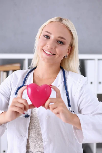 Beautiful smiling doctor hold in arms red heart