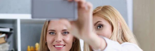 Duas mulheres de negócios no escritório sorriem e fazem selfie — Fotografia de Stock