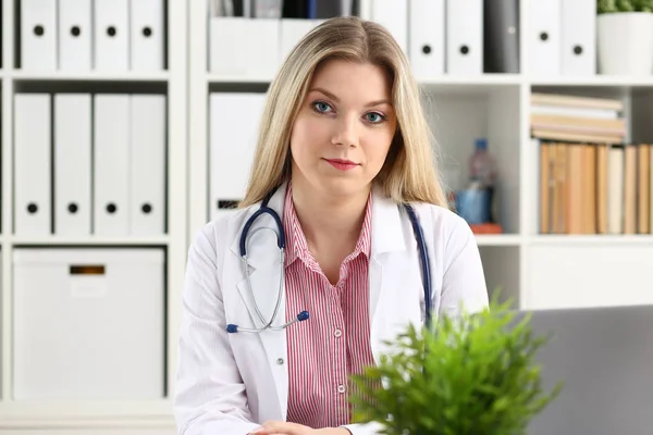 Szép női orvos sit munkahelyen mosolyogva — Stock Fotó
