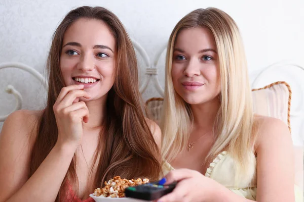 Two happy smiling girlfriends eat popcorn in bed