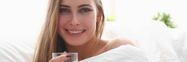 Blonde vrouw houd glas water in arm vroege ochtend verblijf in bed — Stockfoto