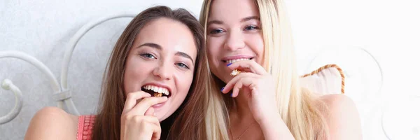 Dos amigas sonrientes felices comen palomitas de maíz en la cama —  Fotos de Stock